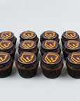 Twelve chocolate cupcakes arranged in two rows on a light gray background, each topped with dark chocolate frosting and a circular topper featuring a gold and purple Brisbane Broncos logo.