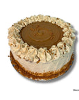 A round Biscuit Torte cake with a glossy brown caramel-like center, piped cream frosting, and cookie crumbs, shown on a white background with the text 'Biscoff Torte' in the bottom right corner.