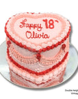 Heart-shaped birthday cake with pink frosting and red accents, featuring 'Happy 18 Olivia' on a white background.