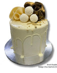 White drip cake with chocolate swirls and balls on a silver cake stand