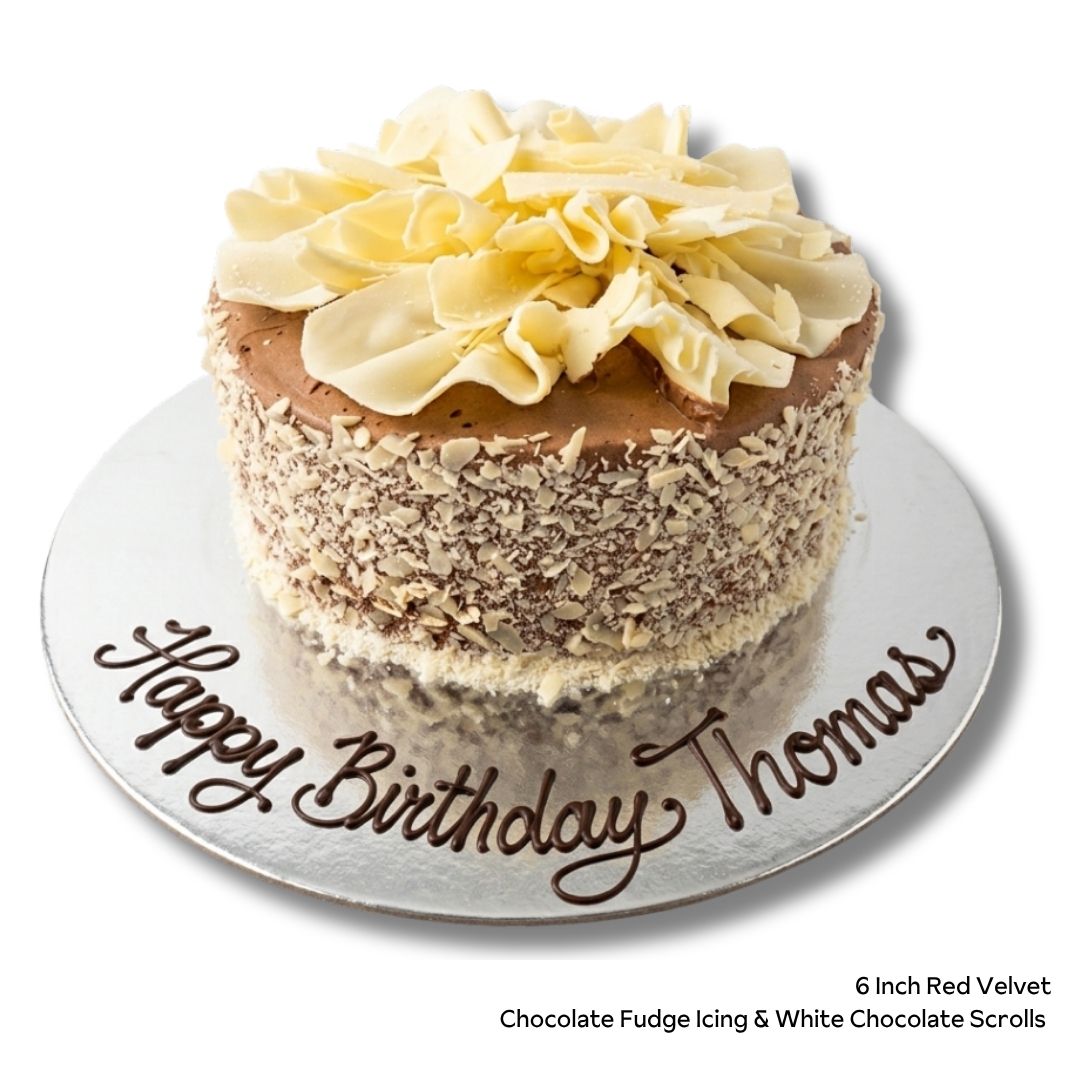 Red velvet birthday cake with chocolate icing and white chocolate sides and scrolls on top. Message written in chocolate 'happy birthday thomas'
