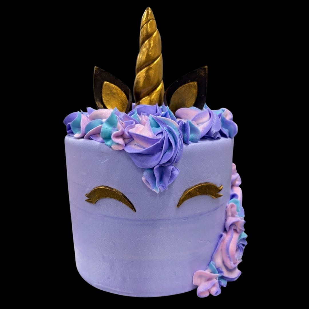 A decorated unicorn-themed cake with a light lavender body, gold horn and closed-eye details, and purple, blue, and pink piped frosting accents on a black background.