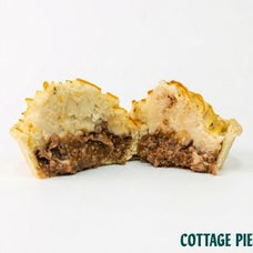 A cut open cottage pie showing a golden-brown pastry crust, a creamy white topping, and a brown meat filling, set against a plain white background with 'COTTAGE PIE' text in the bottom right corner.