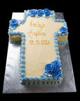 Large cross shaped cake made from carrot cake and cream cheese frosting with piped blue flowers and decorations. 