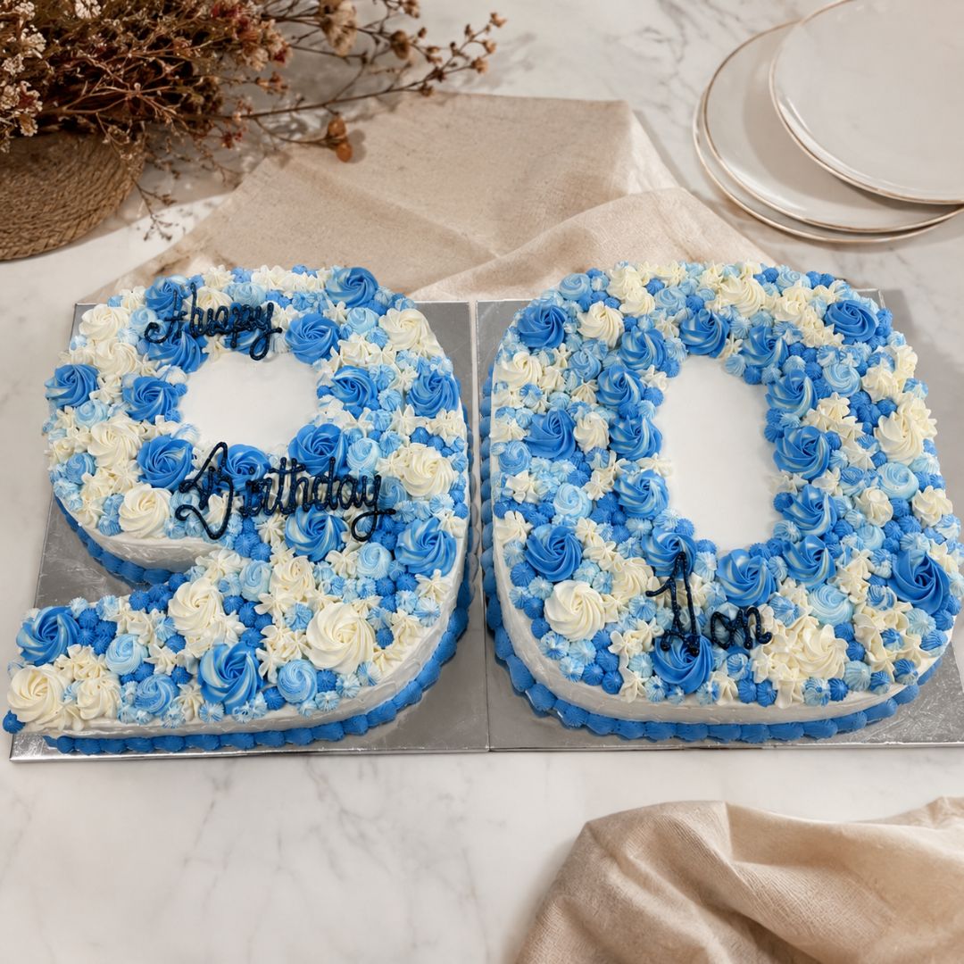 Two floral birthday cakes shaped like the number '90' on a marble surface.