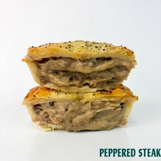 Two stacked halves of a baked stuffed pie or turnover with a golden-brown crust and visible black pepper seasoning, shown on a white background with the text 'PEPPERED STEAK' in the lower right corner.