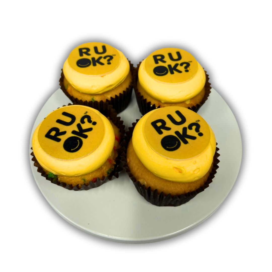 Four cupcakes with yellow icing and 'RU OK?' text on a white plate.