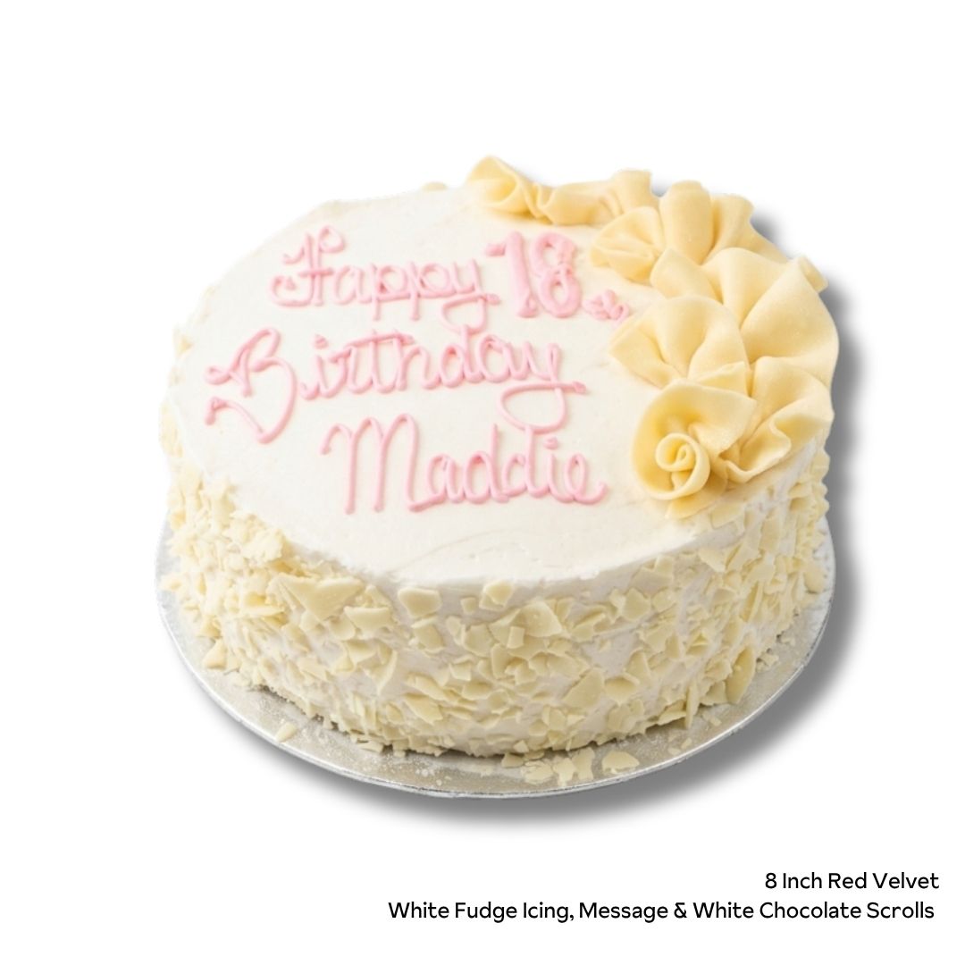A round red velvet cake with cream cheese filling and white chocolate scroll decorations with pink birthday message. 
